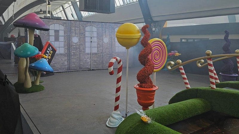Skutečná expozice: poloprázdná hala s betonovou podlahou a několika kulisami lízátek, hub a cukrových hůlek