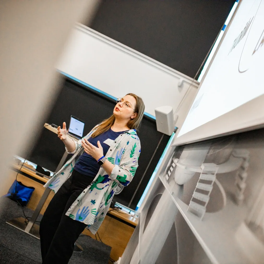 Lenka Stawarczyk vysvětluje účastníkům workshopu, vedle ní plátno s prezentací